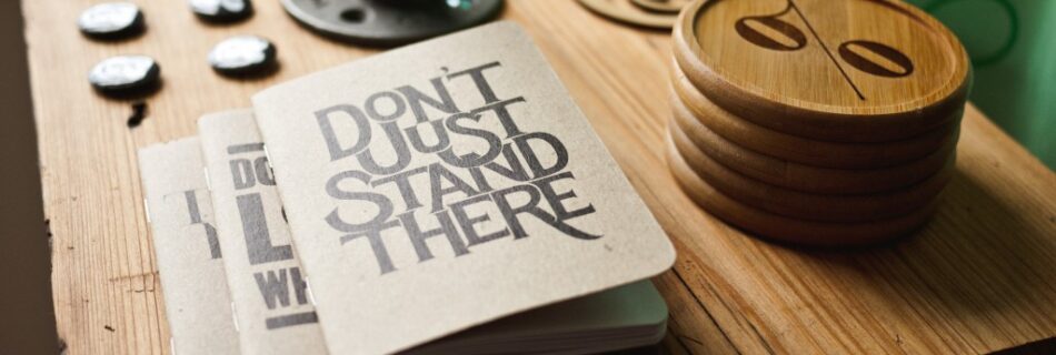 Notebook saying "Don't Just Stand There" on table
